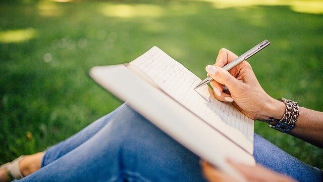 芝生の上で女性がノートに書いている